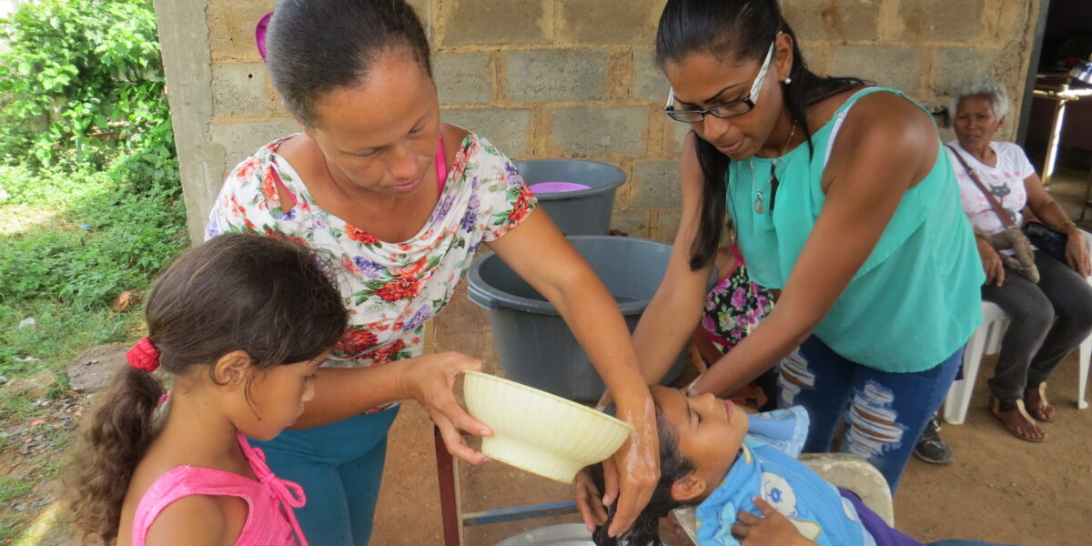 ​Roselyn Rodriguez and Arli Rojas wash Silmarys Rodriguez's hair at Community of Peace Mennonite Church on Isla Margarita. In foreground