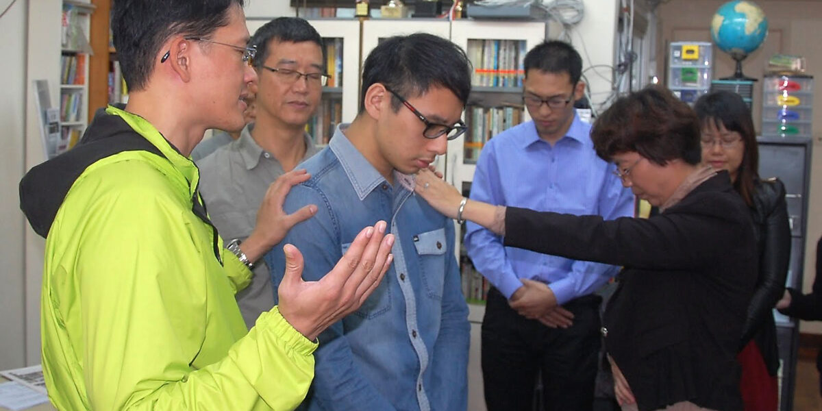 Exchange participants praying for a seminary student from Agape Mennonite Church in Hong Kong. Photo by George Veith. Download full resolution image.