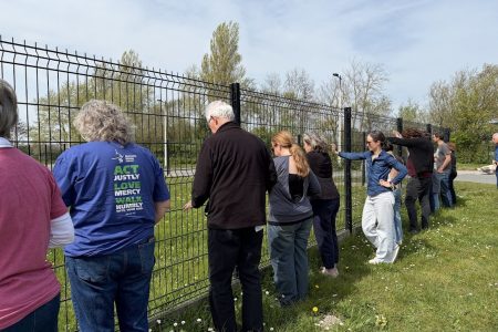 While on a tour of Calais, the pilgrimage stopped to say a prayer while touching one of the many walls put up throughout the city to keep migrating people out. Photo by Roger Farmer.
