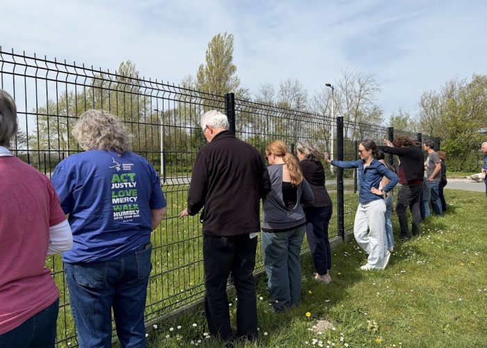 While on a tour of Calais, the pilgrimage stopped to say a prayer while touching one of the many walls put up throughout the city to keep migrating people out. Photo by Roger Farmer.