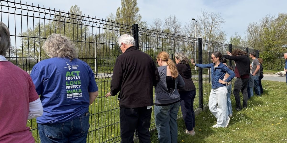While on a tour of Calais, the pilgrimage stopped to say a prayer while touching one of the many walls put up throughout the city to keep migrating people out. Photo by Roger Farmer.