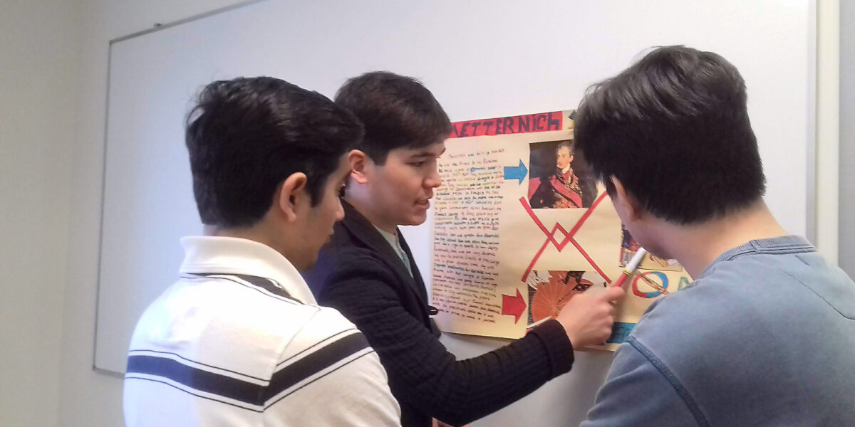 ​This LCC University student from Uzbekistan is explaining his European history poster to his classmates from Afghanistan. (Names withheld for privacy.) Photographer: Robin Gingerich.