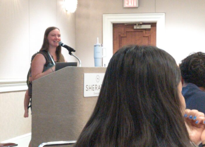 Leigha Stoltzfus, with daughter Naomi napping on her back, addresses attendees at the 'What You Do Next Matters' seminar at Follow Jesus 25. Photo by Travis Duerksen.